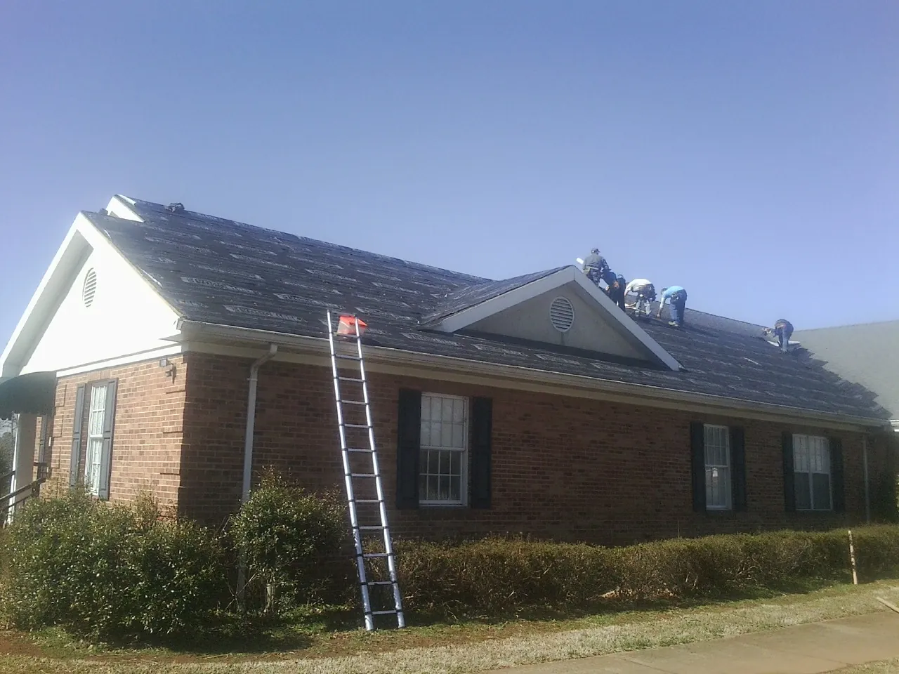 Crew tearing shingles off a brick ranch roof with a ladder set — Emergency Roof Repair work by our crew in Jeddo