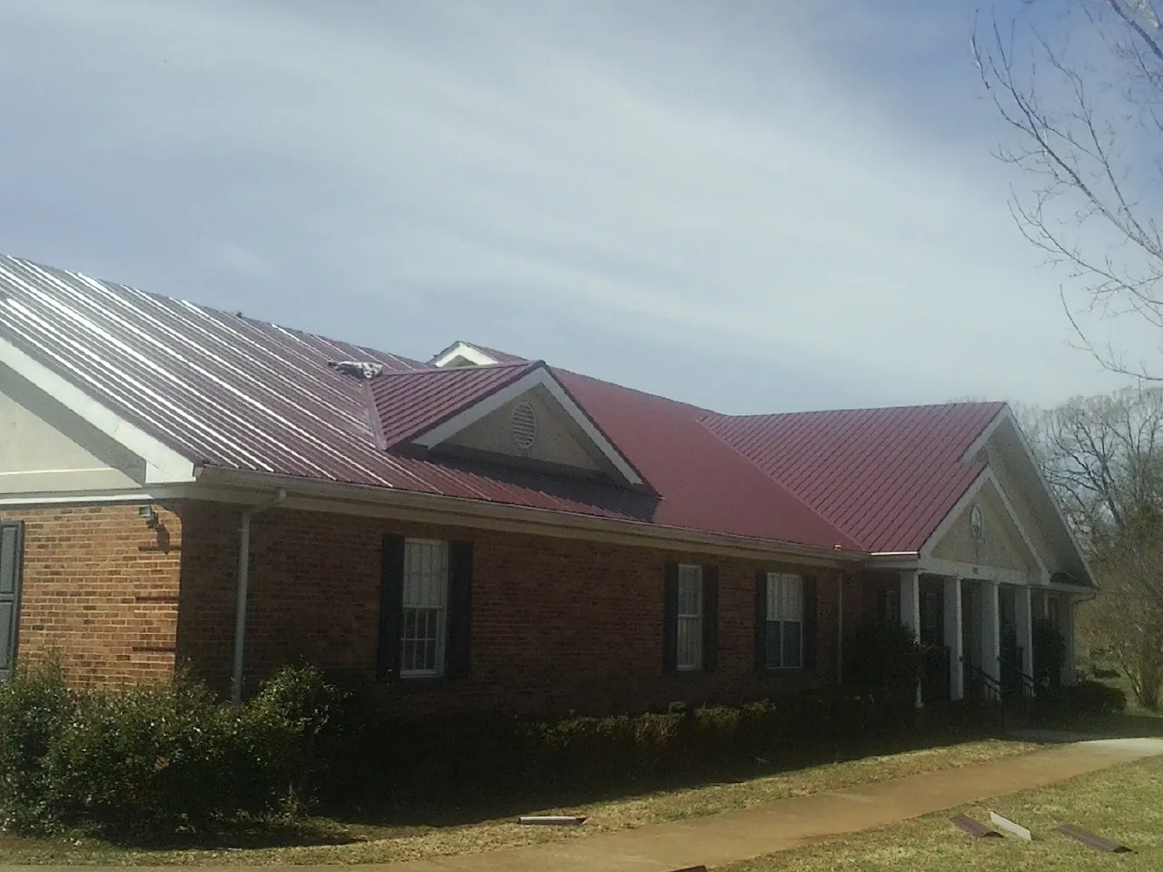 Red metal roof with gabled entries on a long brick building, from a Hail Damage Roof Repair job in Jeddo