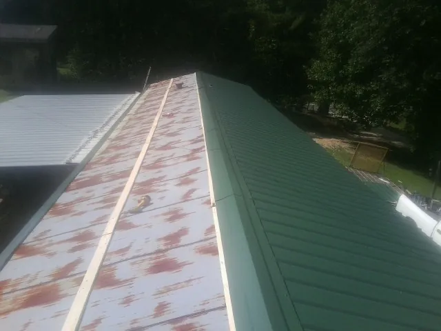 Old rusted panels beside newly installed green metal roofing — Wind Damage Roof Repair by Roofing Brothers in Jeddo