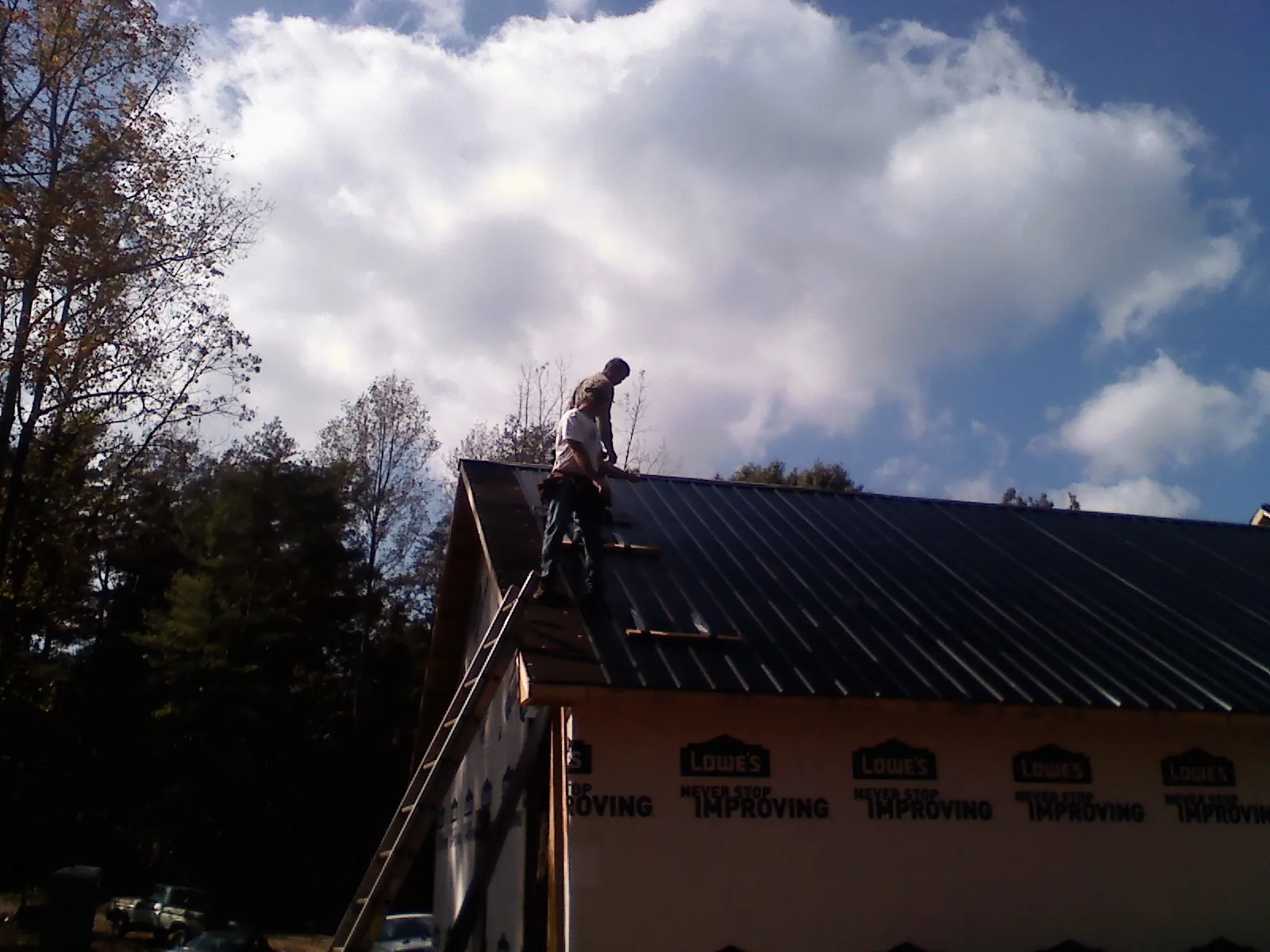 Roofer fastening dark metal panels high against a cloudy sky, from a Roof Inspection job in Jeddo