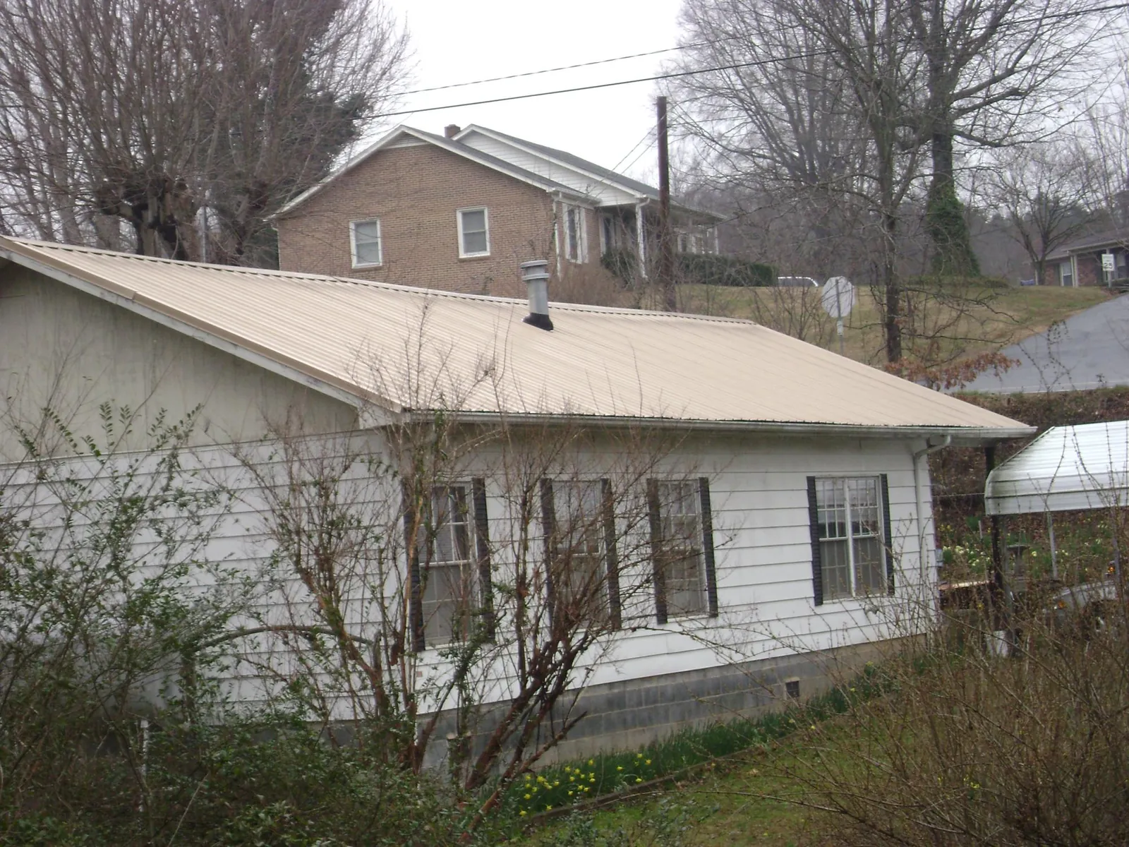 Tan metal roof on a white sided house set into a hillside — Commercial Roofing by Roofing Brothers in Jeddo